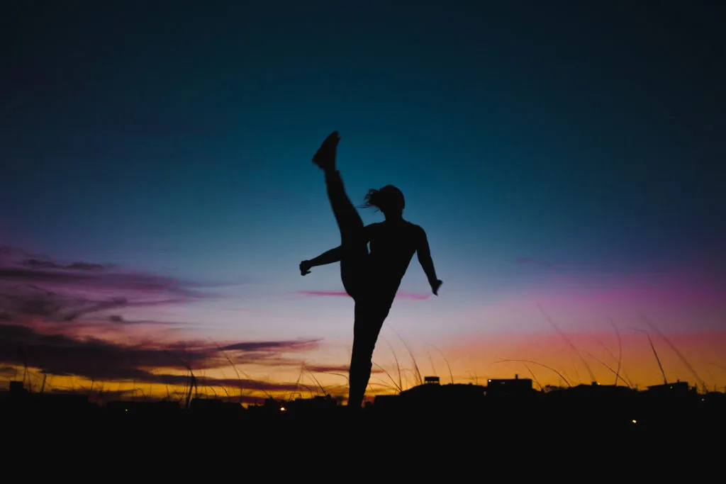 Silhouette of travel girl backpacker doing high-kicks at sunset in Uruguay