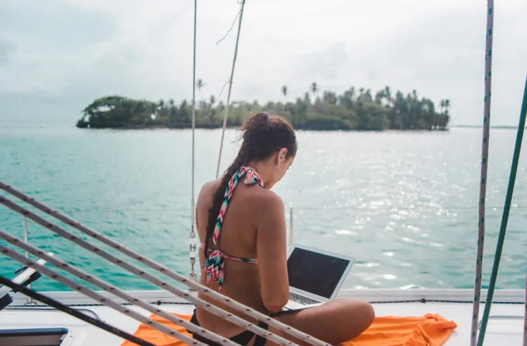 How travel bloggers make money: Remote worker/digital nomad works on laptop on a boat in Caribbean paradise